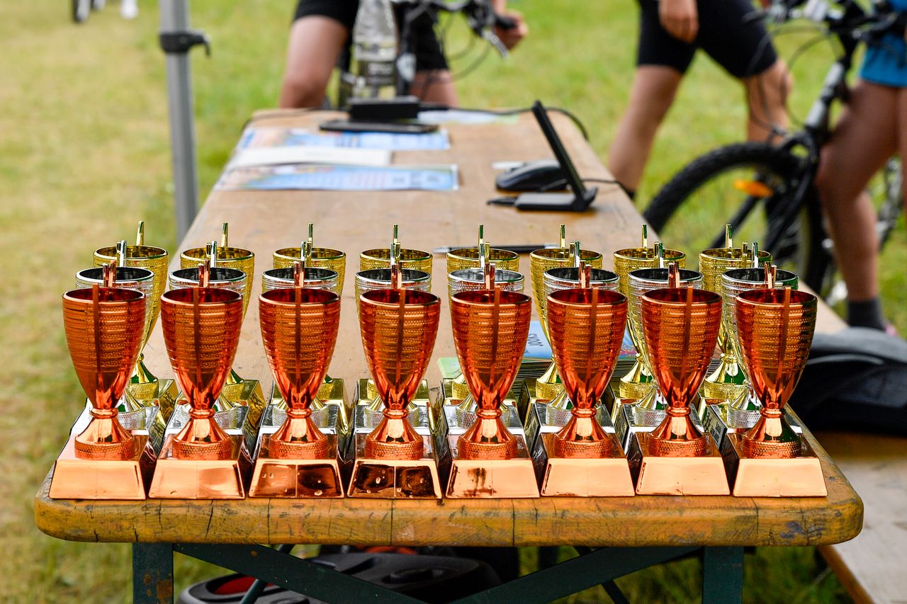 our-journey-03 Bronze and gold trophies displayed on a wooden table at an outdoor cycling event in Estonia.
