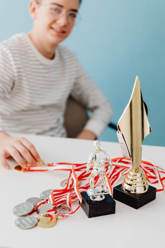 who-we-are Person with trophies and medals on a white table, symbolizing success and achievement.