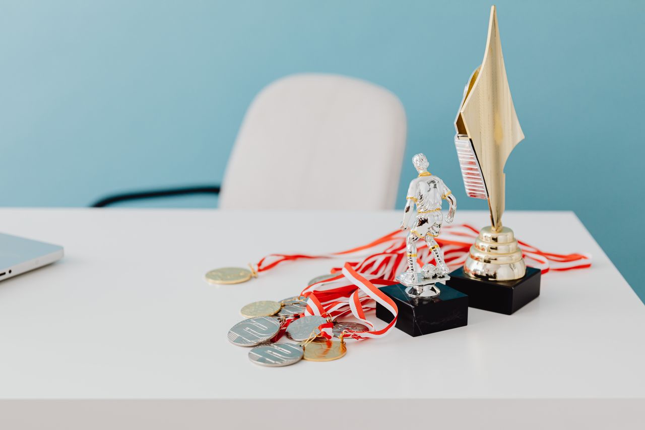 why-choose-us A collection of trophies and medals displayed on a white desk, symbolizing success and victory.