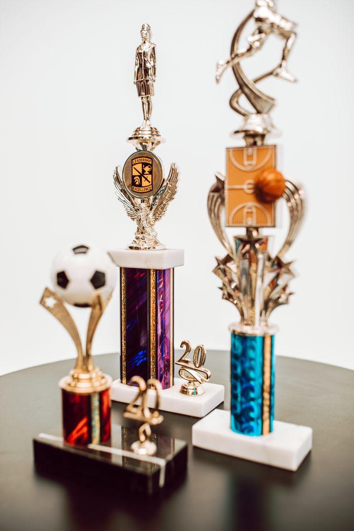 services-01 An assortment of sports trophies featuring different designs and sports, displayed on a table.